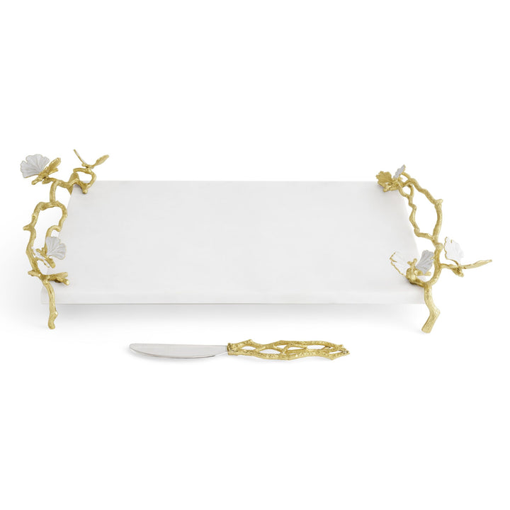 Michael Aram rectangular white marble serving platter with decorative gold branch handles featuring white flower accents, shown on a white background with a matching small knife in front.