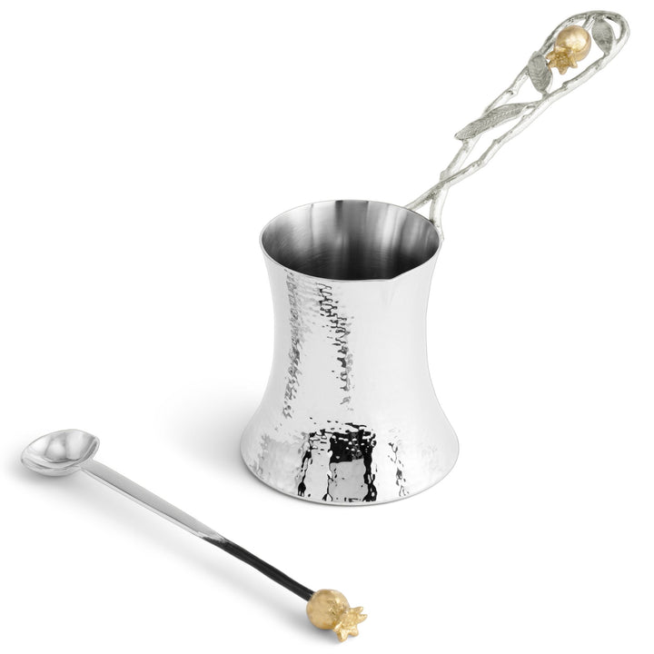 A hammered silver Michael Aram Pomegranate coffee pot with a decorative silver handle featuring gold-toned pomegranate accents, shown alongside a matching long spoon 