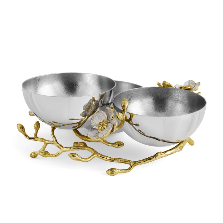 Back angled view of Michael Aram Orchid Triple Low serving Bowl showing three reflective silver-tone bowls nestled within dimensional goldtone orchid branches with white enamel flowers and buds