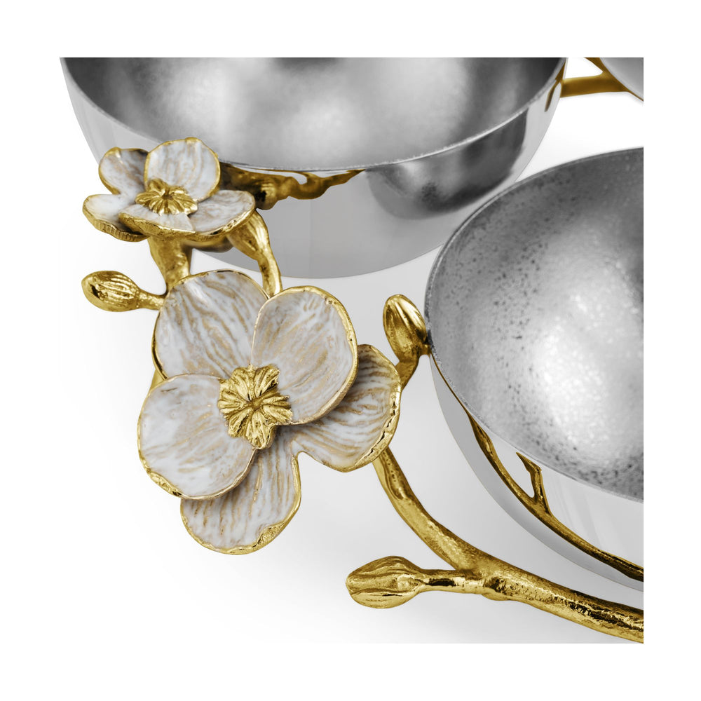Close-up of decorative metal serving pieces with silver bowls and gold branch-and-orchid flower accents 