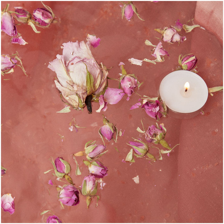 SELV Rituel Quartz Immersive Bath Ritual  shown with contents of kit: floating flowers, rose buds and candle in bath water