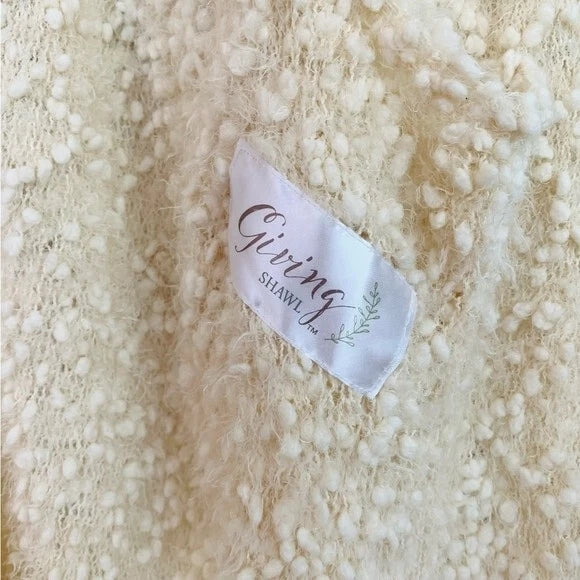Close-up of a textured beige fabric with a 'Co Giving Shawl' tag.
