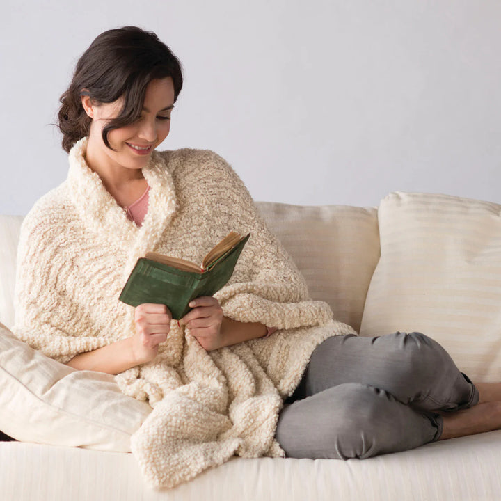 Woman reading a book wrapped in her cozy  giving shawl on the couch