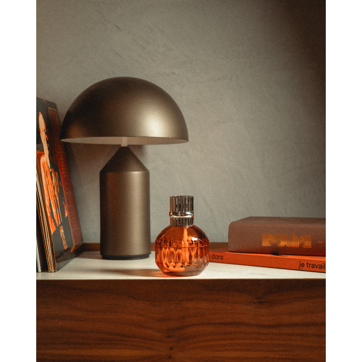 Lampe Berger Cannelo Paprika lamp in warm amber-orange fluted glass with a silver-coloured slotted diffuser top, displayed beside books and a table lamp.
