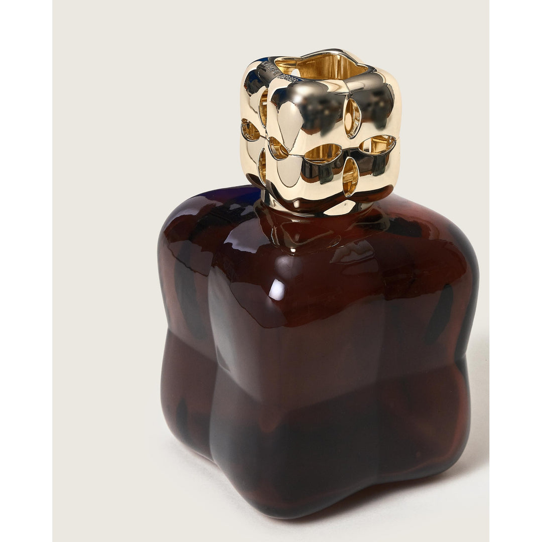 Lampe Berger Cosy Plum home fragrance lamp in deep plum glass with softly undulating sides with a gold-coloured diffuser cap with oval cut-outs, on a beige background
