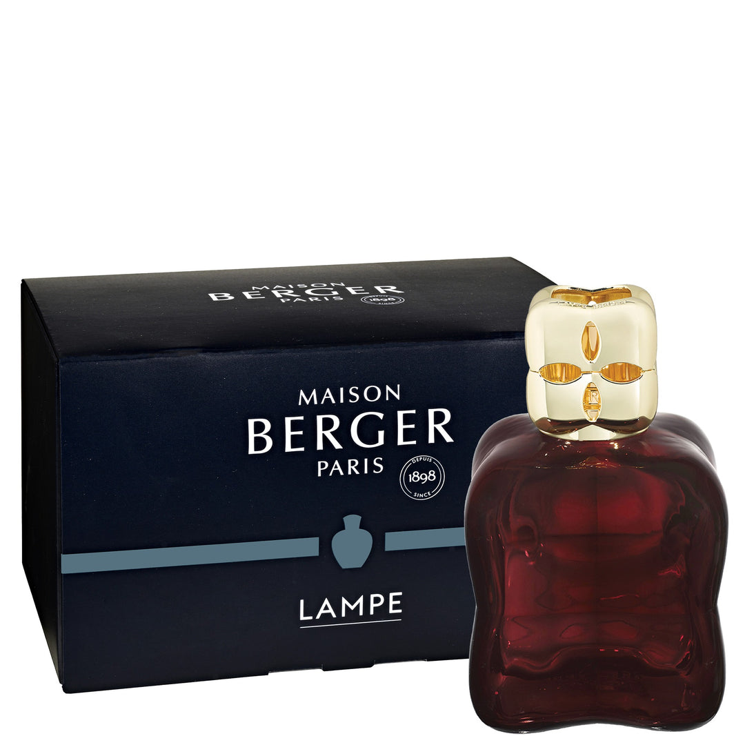 Lampe Berger Cosy Plum home fragrance lamp in deep plum glass with softly undulating sides with a gold-coloured top with oval cut-outs, beside its dark Maison Berger box.
