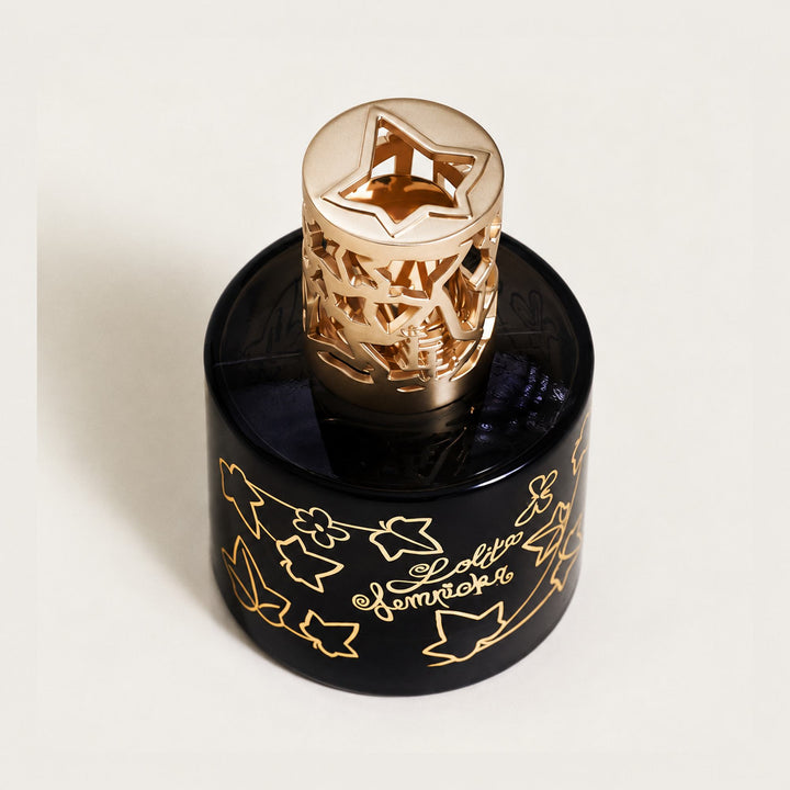 Top view of the black Lampe Berger Lolita Lempicka lamp and its decorative gold-coloured diffuser top, showing the ivy leaft motif on the bottle is the same motif on the special diffuser cap

