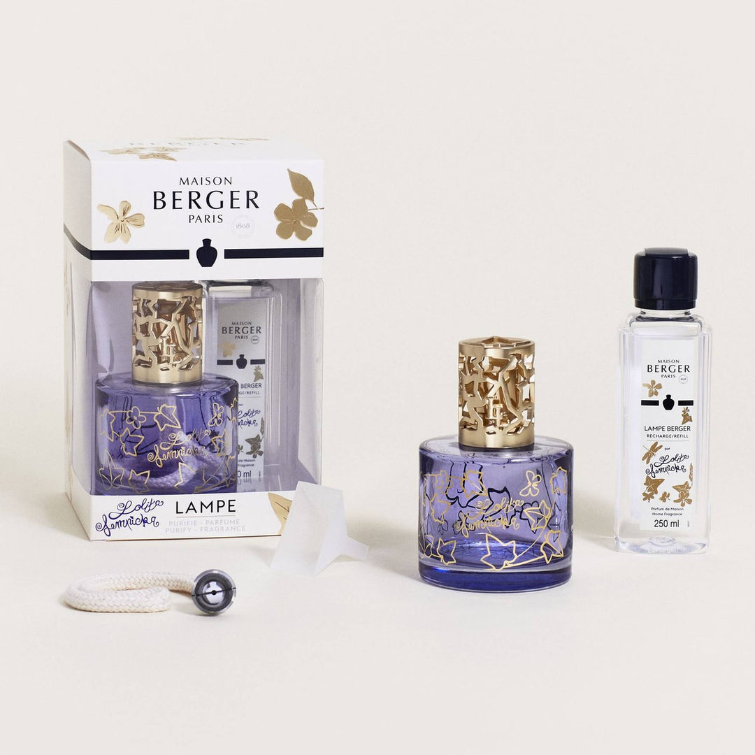 Lampe Berger Lolita Lempicka home fragrance lamp with a cylindrical violet-blue glass body, gold ivy-leaf outlines and Lolita Lempicka script, topped by a satin-gold ivy-cutout diffuser cap, displayed with its matching 250 ml refill, white wick-burner, translucent funnel and floral presentation box.
