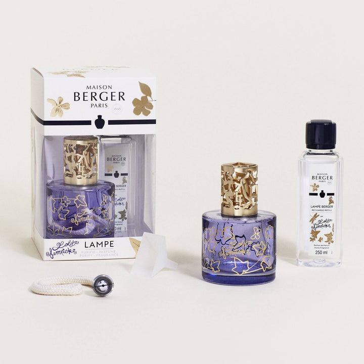 Lampe Berger Lolita Lempicka home fragrance lamp with a cylindrical violet-blue glass body, gold ivy-leaf outlines and Lolita Lempicka script, topped by a satin-gold ivy-cutout diffuser cap, displayed with its matching 250 ml refill, white wick-burner, translucent funnel and floral presentation box.

