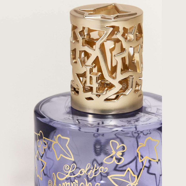 Close-up of the Lampe Berger Lolita Lempicka violet-blue glass lamp, highlighting the gold ivy vines, signature script and satin-gold metal diffuser cap with ivy-shaped cutouts.
