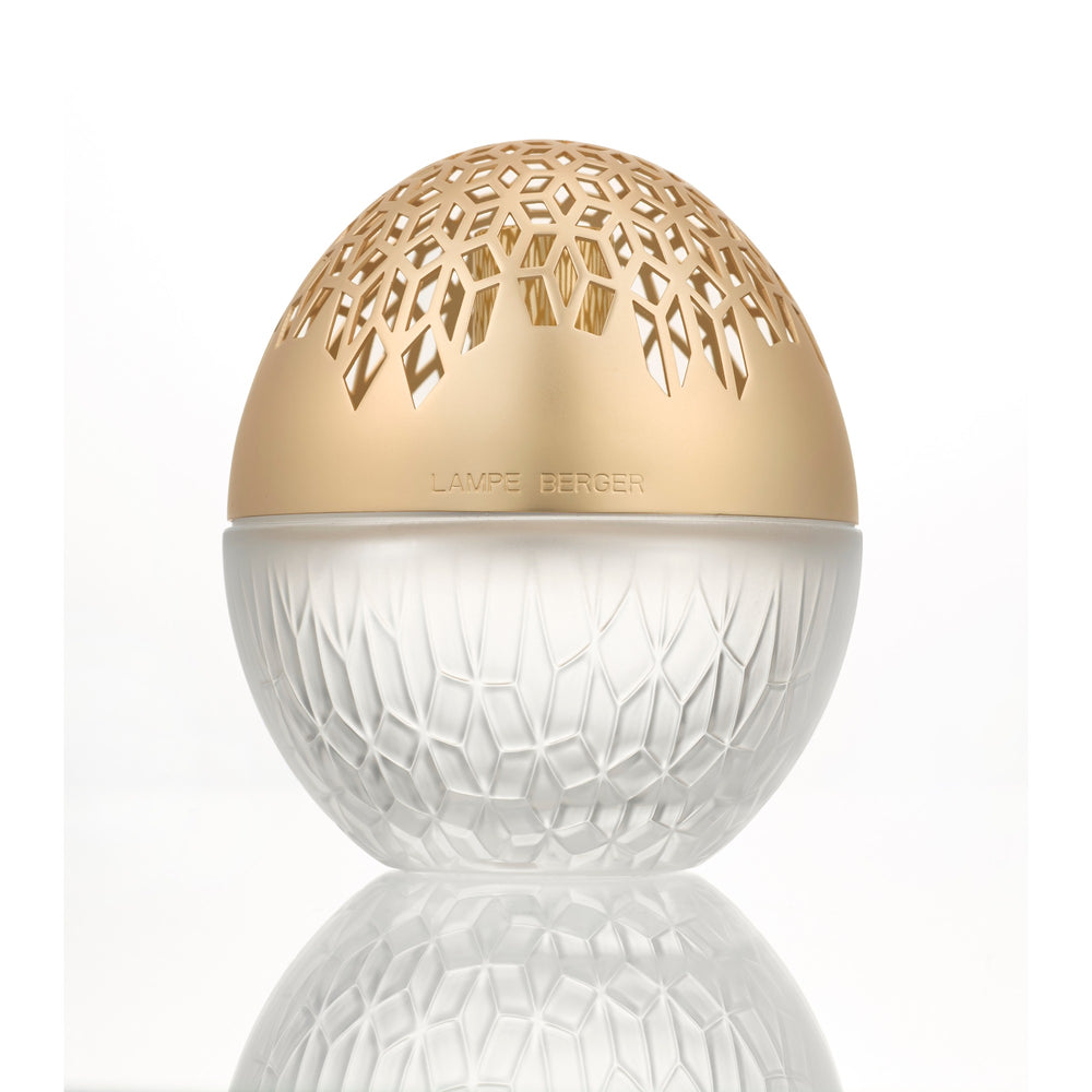 Lampe Berger Luka Oval Frosted home fragrance lamp in frosted white patterned glass with a warm gold-toned domed top with geometric cut-outs, reflected on the surface below.
