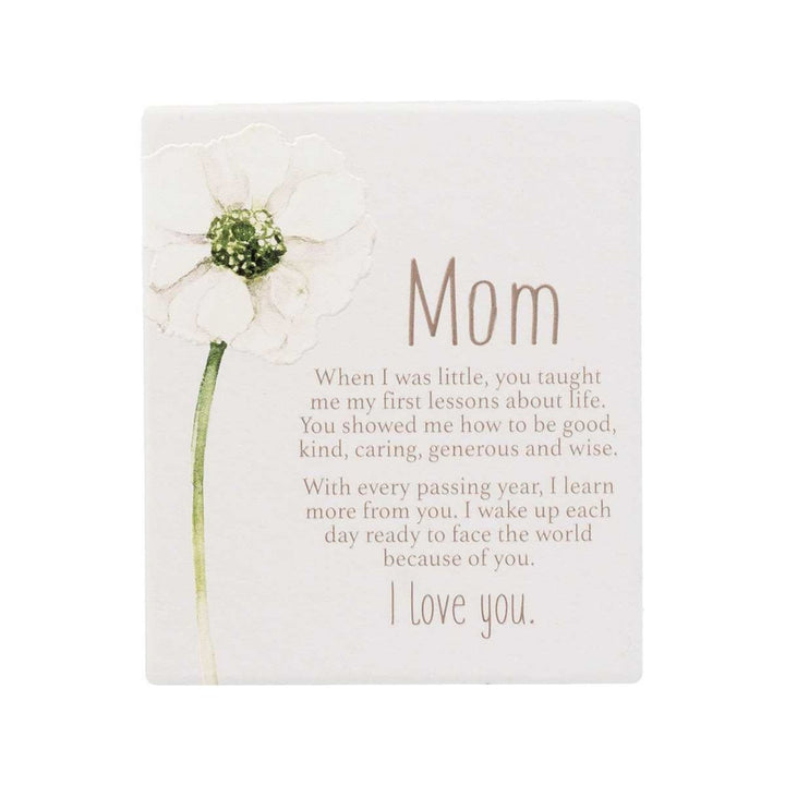 A rectangular white memorial-style easel plaque with a large white flower illustration on the left and a touching poem addressed 'Mom' in brown lettering, shown on a plain white background.